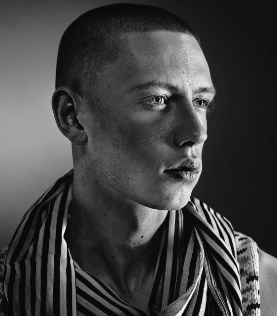Portrait of a young adult male with short hair wearing a striped shirt. The image is black and white and the man is looking off to the side.