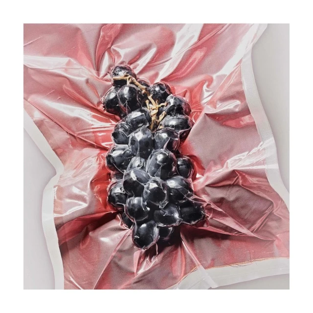 Close-up of a bunch of fresh, dark grapes vacuum-sealed in pink plastic packaging, set against a clean, neutral background.