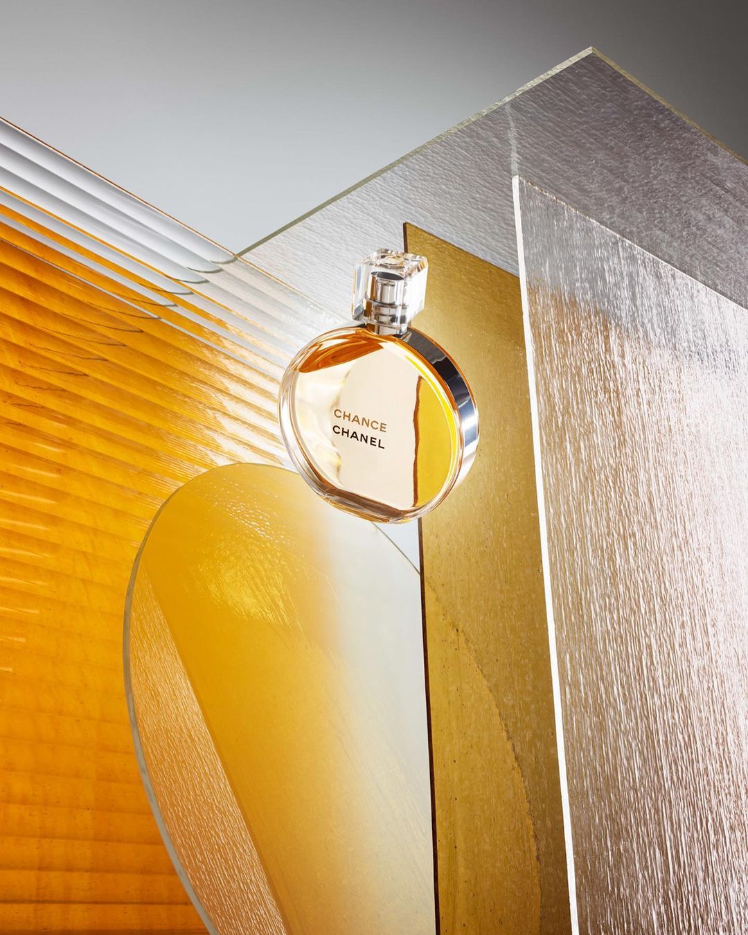 Close-up of a Chanel Chance perfume bottle against clear and gold abstract geometric shapes in a beauty or fashion shot.
