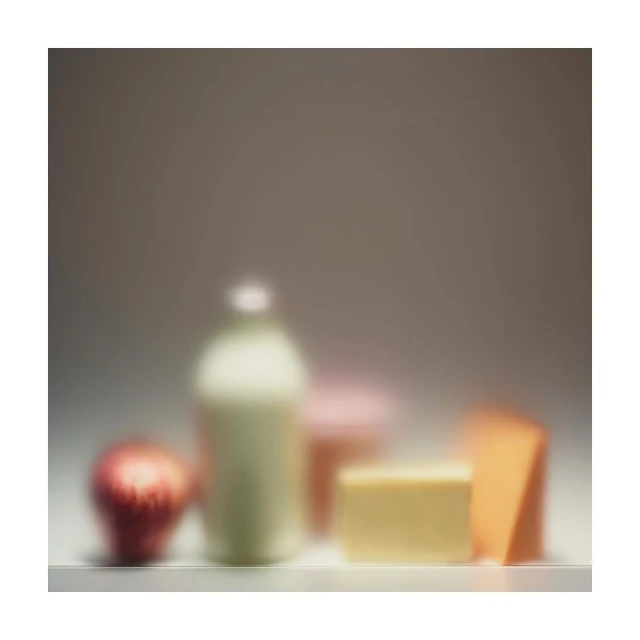 Still life photo of an apple, a bottle of milk, and blocks of cheese in soft focus, presenting a minimalist food composition.