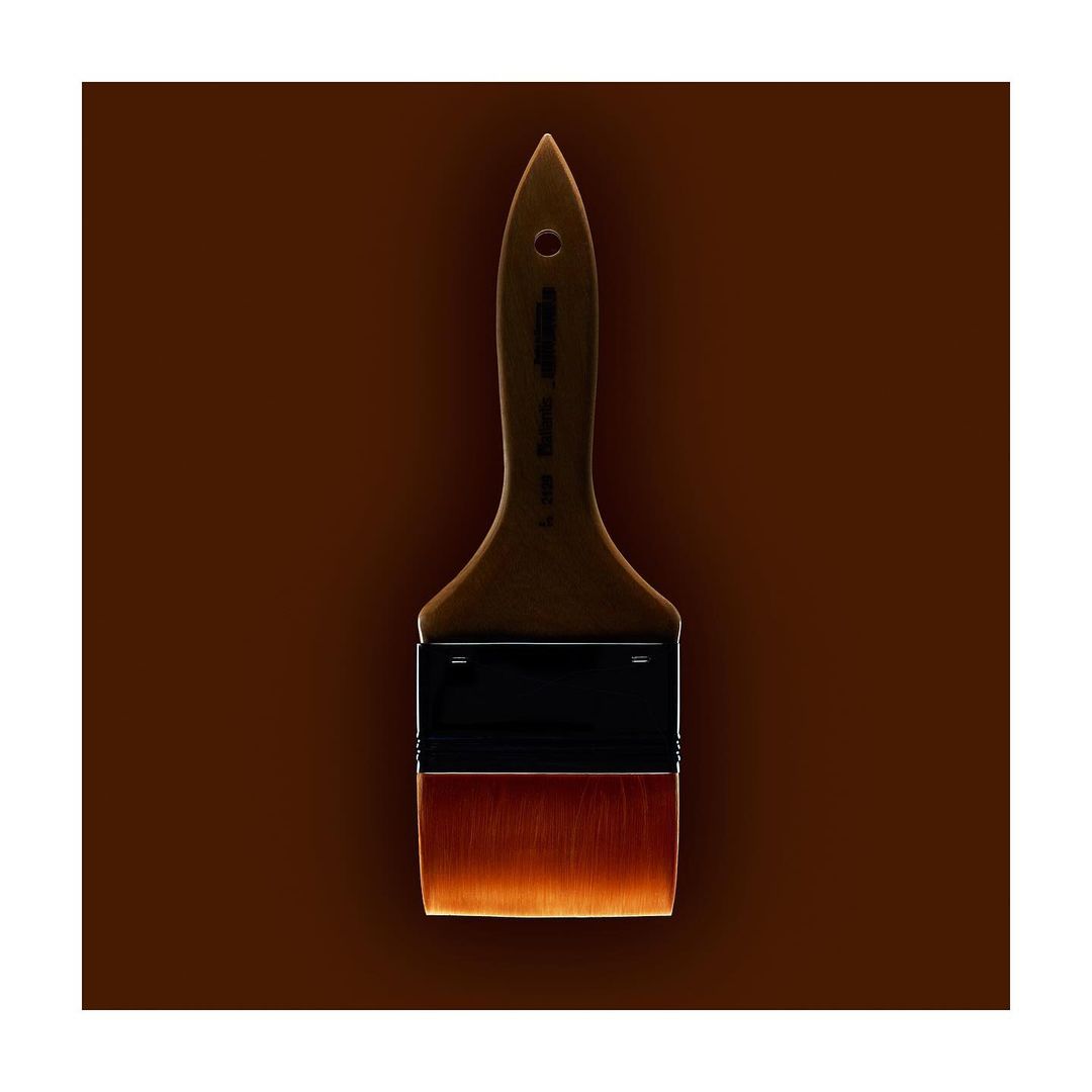 Angled shot of a paint brush with brown bristles and a brown handle on a brown background, showcasing simple composition and warm tones.