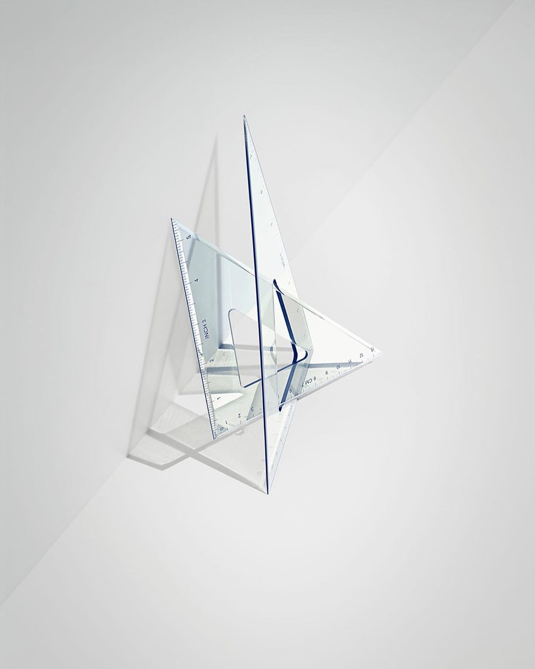 Transparent plastic set square and triangle placed on a white surface with cast shadow, photographed in a minimalist, clean style.