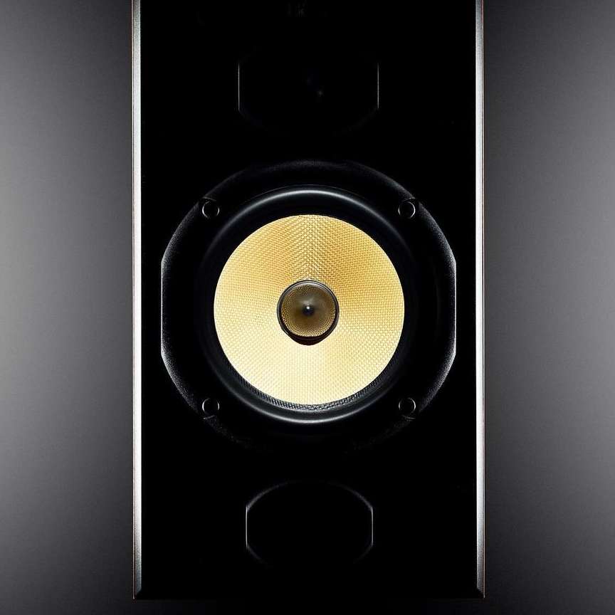 Close-up of a sleek, black speaker with a central yellow driver, showcasing modern audio equipment design.