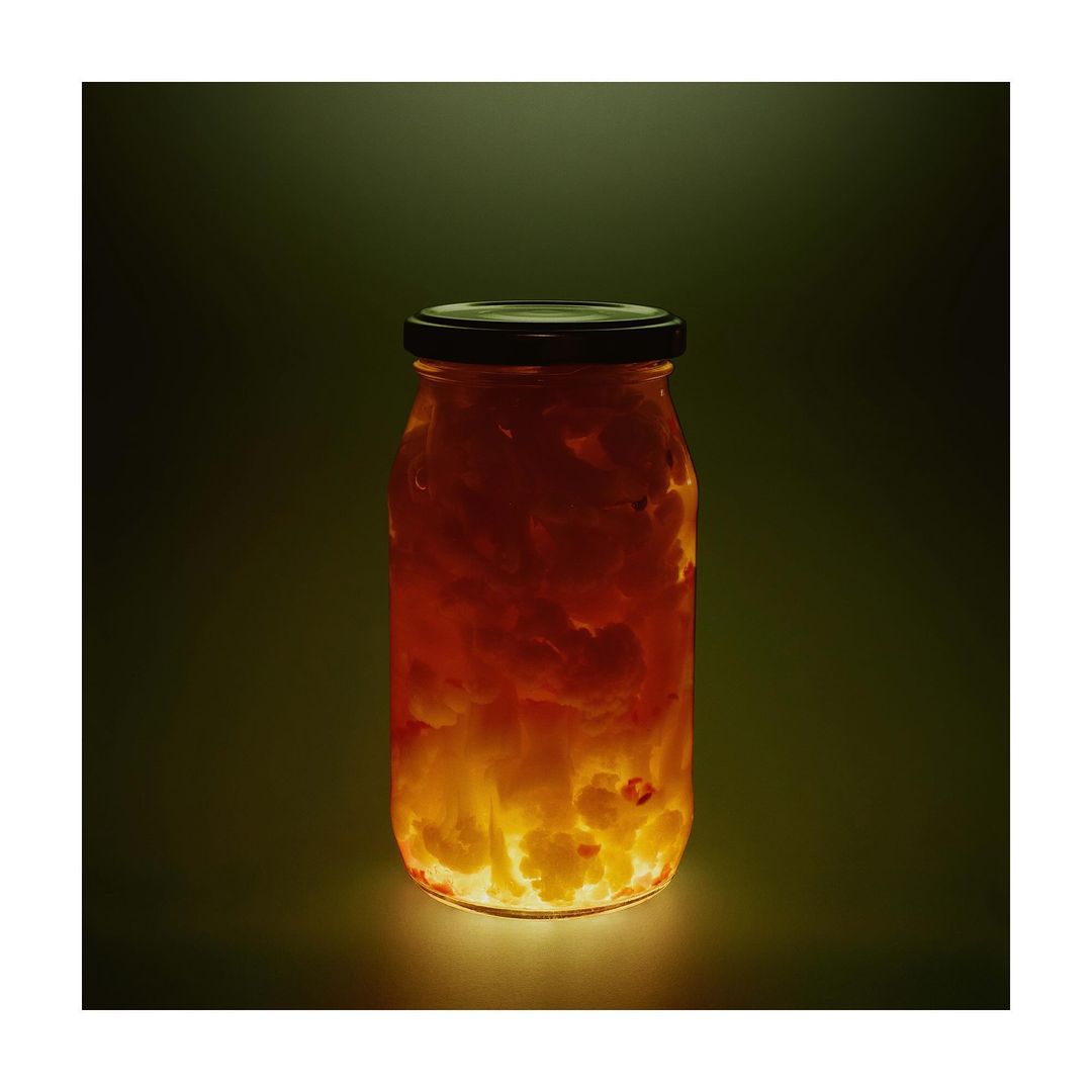 A vibrant glass jar filled with a translucent, golden preserve, lit from below against a moody, dark green background, studio food photography.