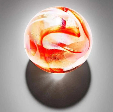 Close-up of a translucent orange and white swirl marble casting a shadow on a grey surface in a studio shot. Toy, collectible.