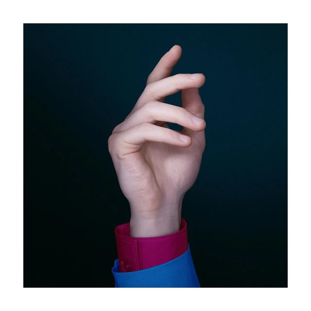 Close-up studio shot of an adult hand with fair skin, wearing a blue shirt with pink cuffs, against a dark green backdrop.