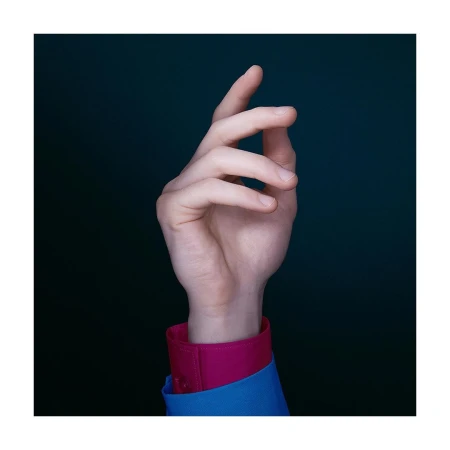 Close-up studio shot of an adult hand with fair skin, wearing a blue shirt with pink cuffs, against a dark green backdrop.