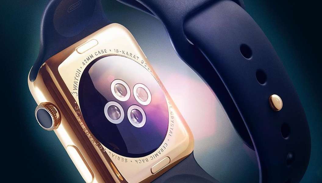 Close-up of a gold smartwatch with a black band shows the sensors on the back casing and the band attachment button detail.