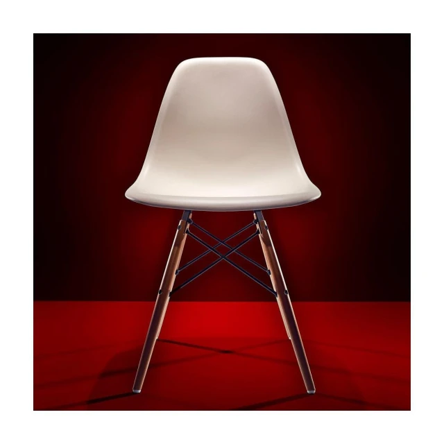 A studio shot of a modern white plastic chair with wooden legs against a graduated red background.