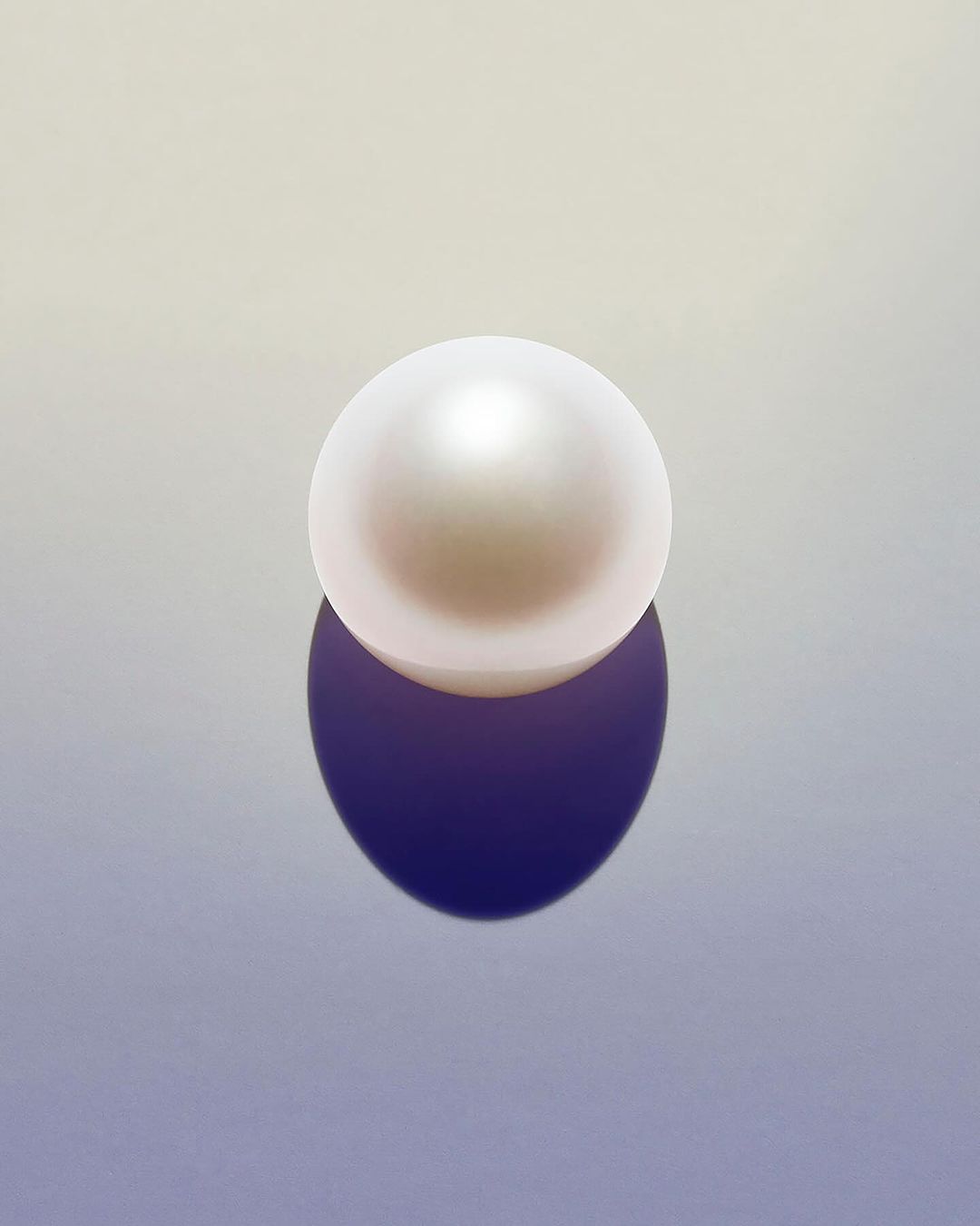Luminous white pearl with a dark purple reflection on a smooth graduated backdrop in white and light blue creating a soft lighting effect.
