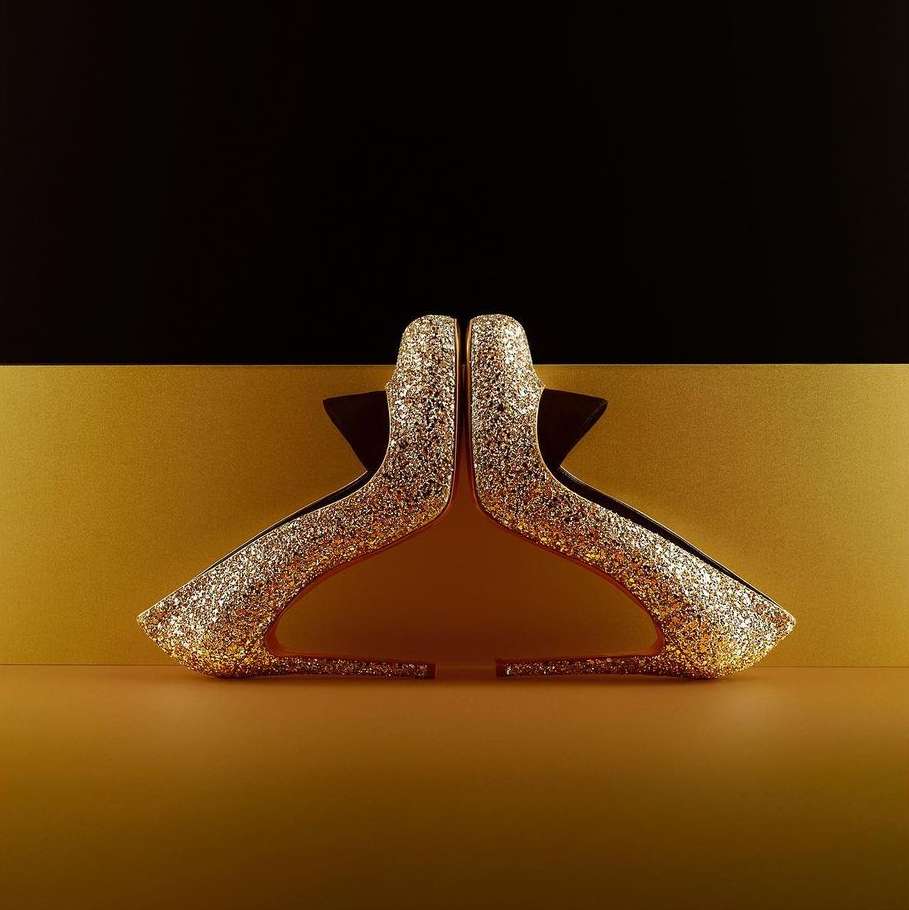 Glittering gold high-heel shoes are displayed against a modern background in black and gold creating a visually striking image.