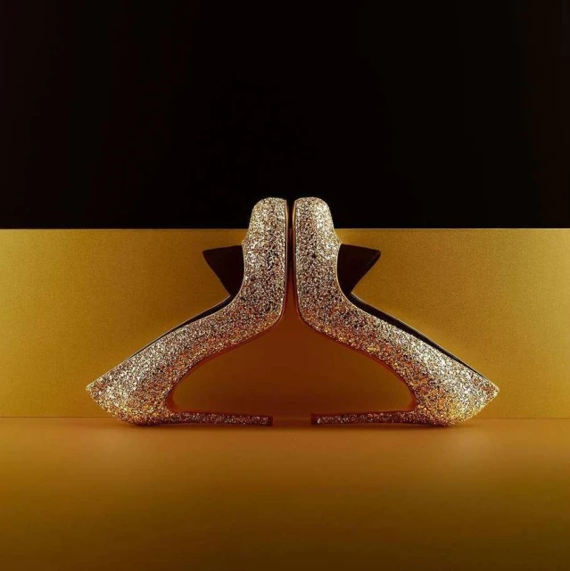 Glittering gold high-heel shoes are displayed against a modern background in black and gold creating a visually striking image.