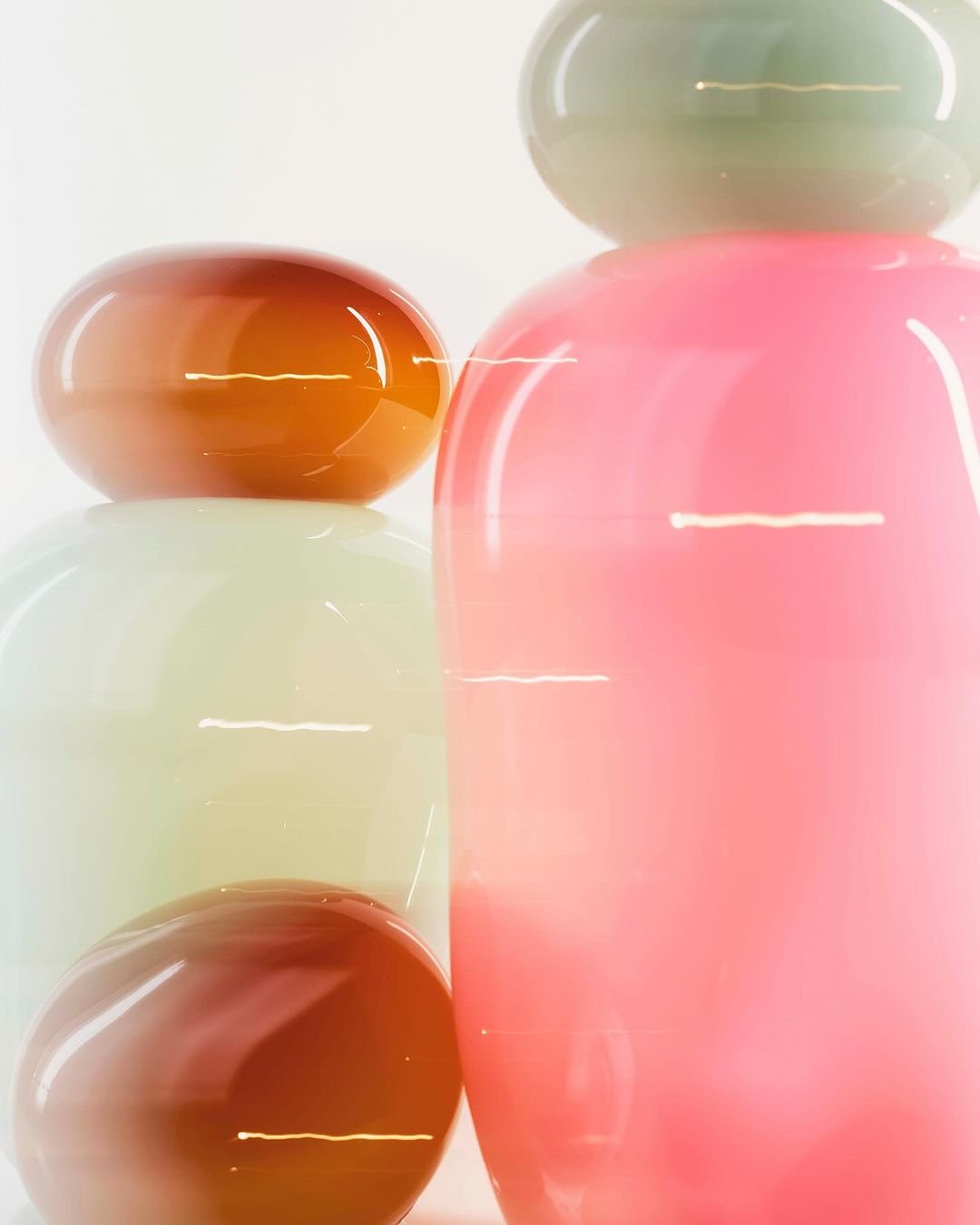 Stacked glass sculptures in pink, orange, green, and white hues, showcasing a modern art aesthetic against a clean, bright background.