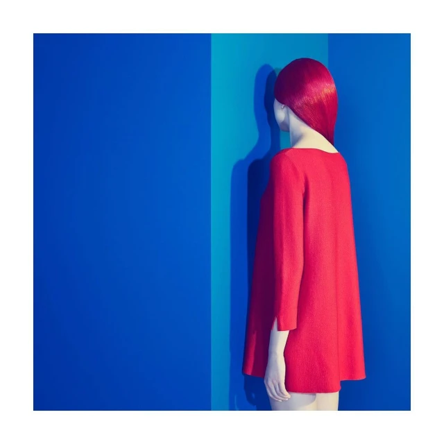 Woman in a red dress stands against a backdrop of vertical blue and teal stripes in a studio fashion shot.