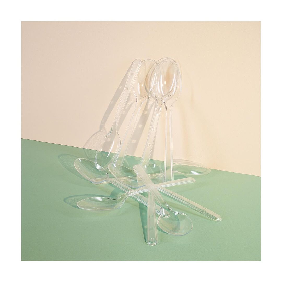 Still life shot of a collection of transparent plastic spoons against a cream and seafoam-green background creating shadows and reflections.