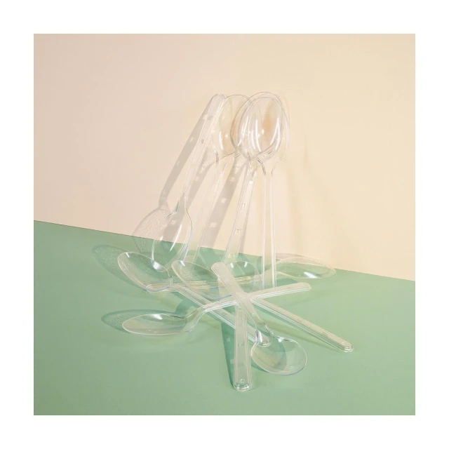 Still life shot of a collection of transparent plastic spoons against a cream and seafoam-green background creating shadows and reflections.