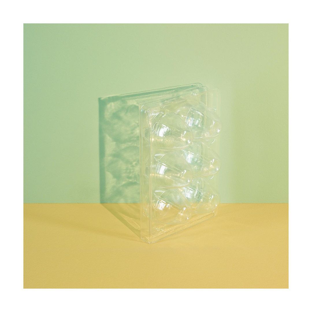 Close-up studio shot of a transparent plastic egg carton against a backdrop featuring light green and yellow-beige color-blocked sections.