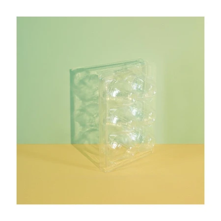 Close-up studio shot of a transparent plastic egg carton against a backdrop featuring light green and yellow-beige color-blocked sections.