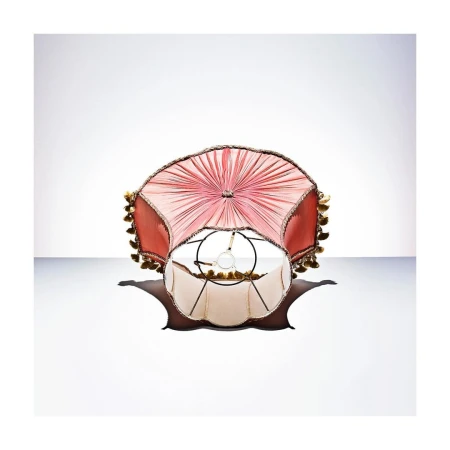 Close-up shot of an ornate lampshade with a salmon pink fabric shade and ivory interior, casting a soft shadow on a white background.