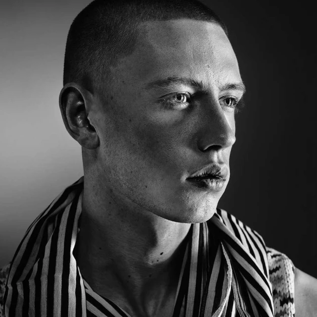 Monochrome portrait of an adult male with a close-cropped haircut, wearing a striped scarf, and captured in a photo studio setting.