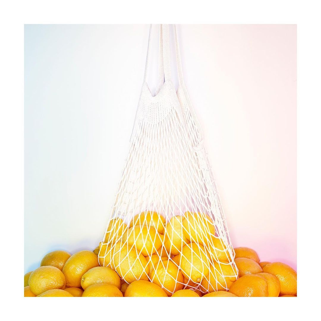 Close-up of a white string bag filled with lemons against a white background, showcasing a healthy and sustainable food choice.