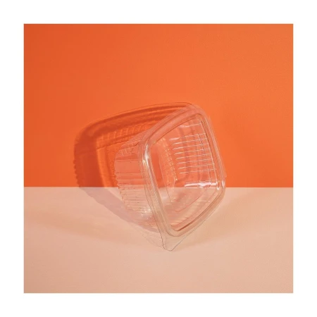 Clear plastic clamshell container on peach surface against orange background with shadow indicating studio or artificial lighting.