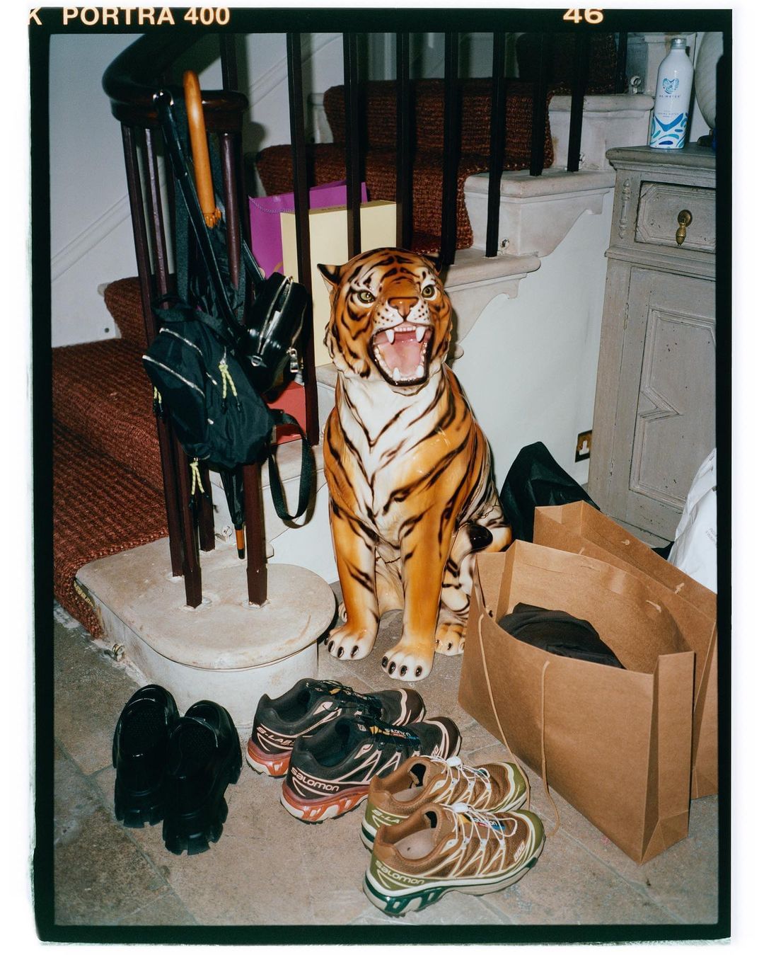Still life shot: Tiger statue, bags, umbrella, and shoe collection arranged inside a home, casting a light-hearted and domestic mood.