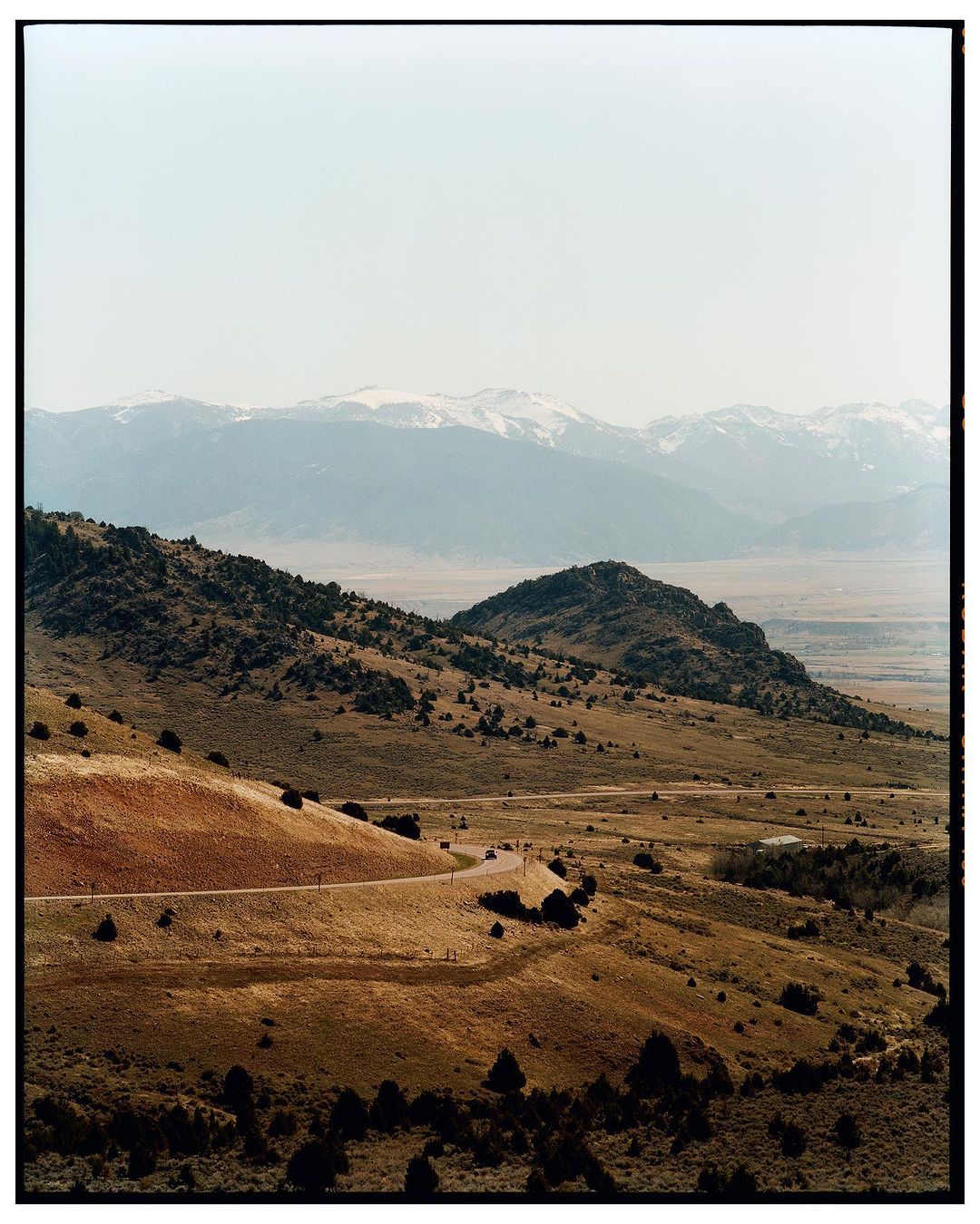 Vast landscape showcasing rolling hills, dry terrain, and distant snow-capped mountains under a clear sky, capturing a sense of natural grandeur.