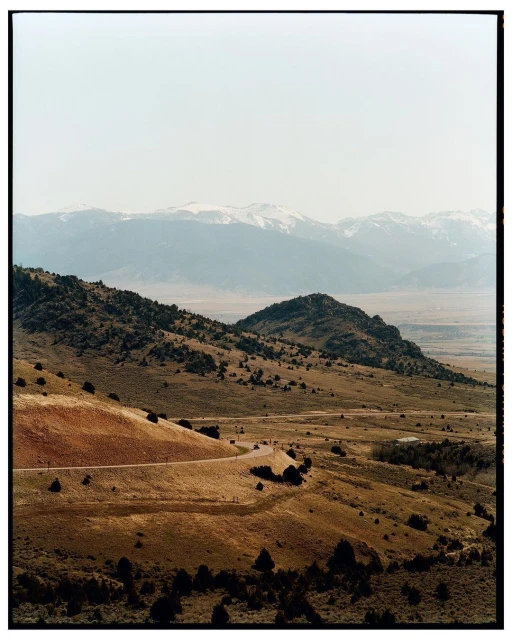 Vast landscape showcasing rolling hills, dry terrain, and distant snow-capped mountains under a clear sky, capturing a sense of natural grandeur.