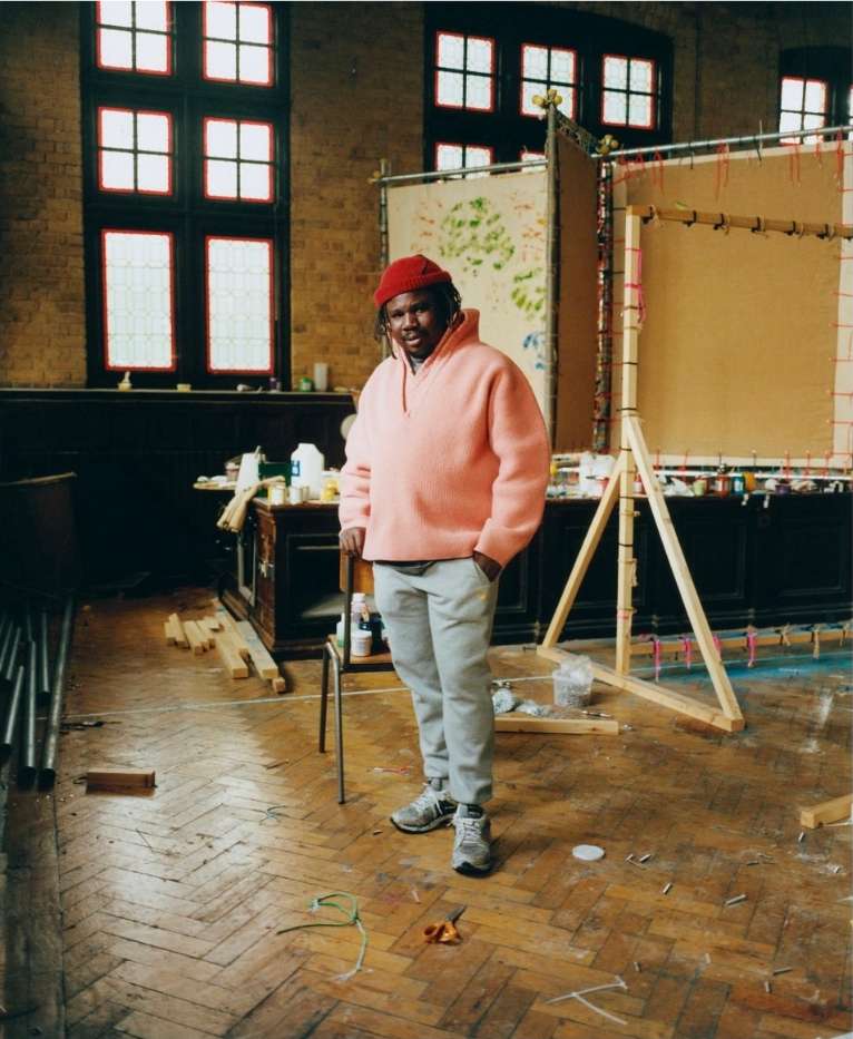 Portrait of an African American artist in a pink sweater and red hat standing in a studio space with easels and art supplies, indoor.