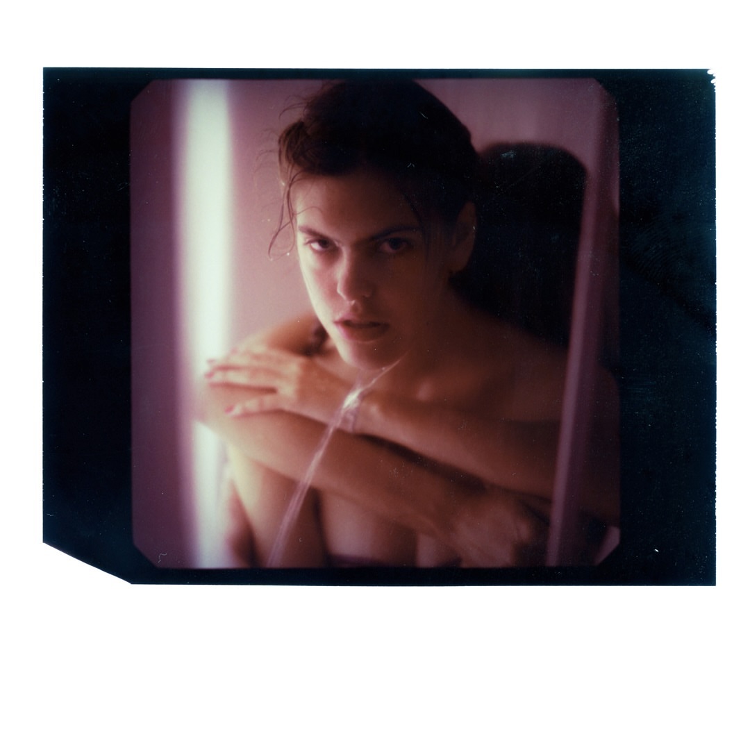 Portrait of a person with crossed arms, set against a blurred background. The image shows a tight crop and intimate studio setting.