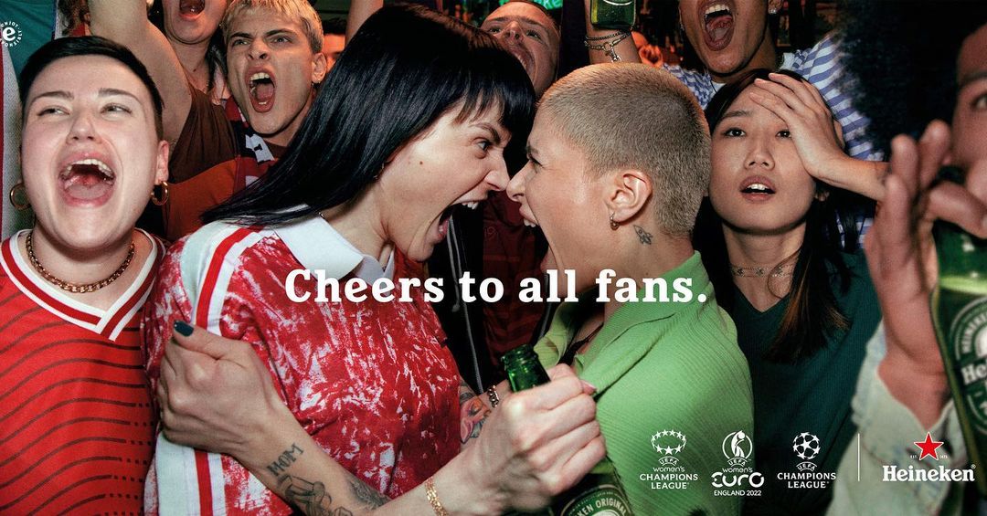 Energetic shot of beer advertisement featuring diverse fans shouting, holding Heineken bottles, with visible text 'Cheers to all fans'.