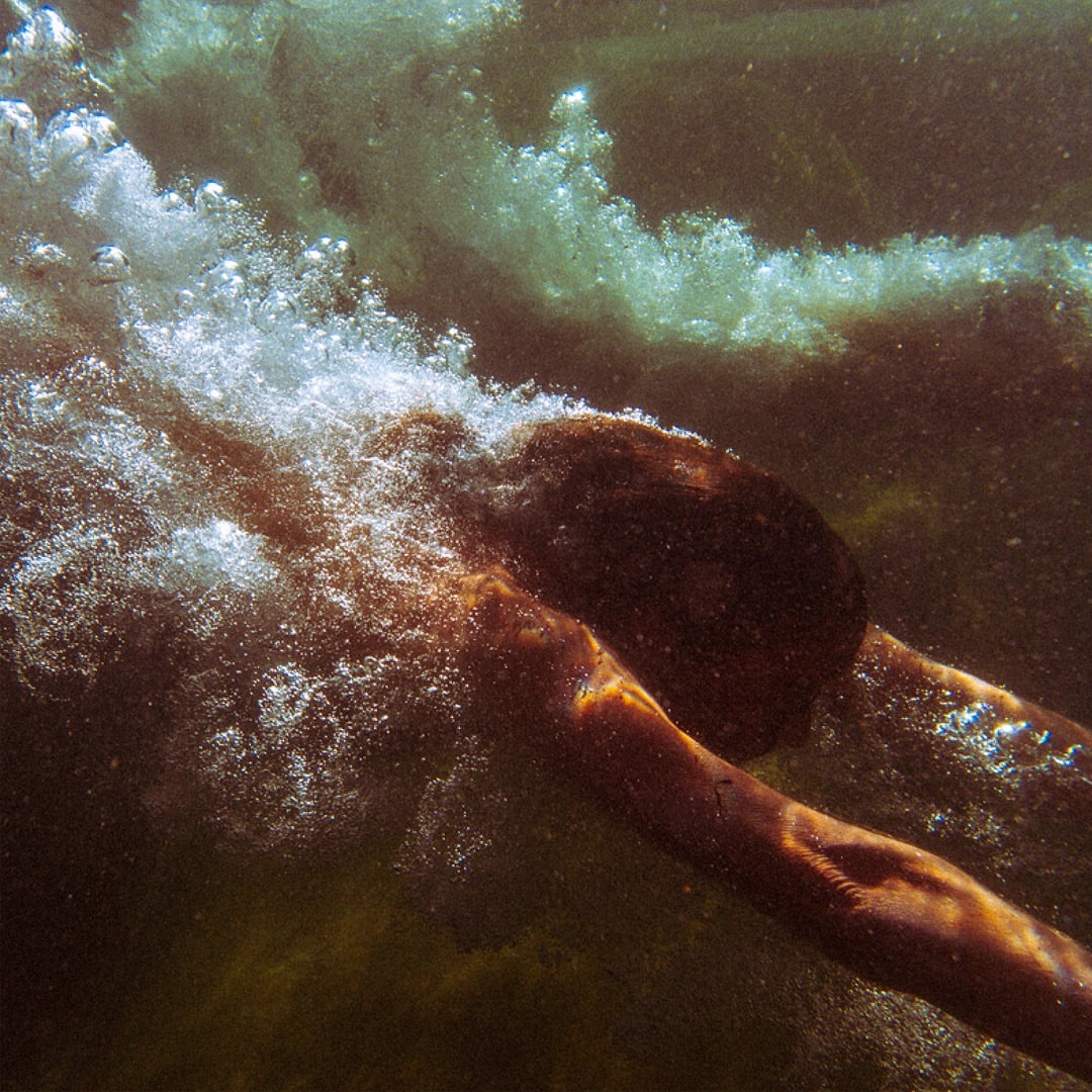 Underwater view of a person swimming, bubbles rising toward the surface, with diffused natural lighting creating a dynamic aquatic scene.