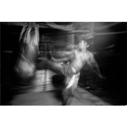 Monochrome action shot of a martial artist kicking a heavy punching bag with heavy motion blur in a dim training space