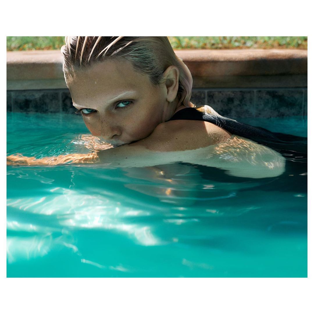 Blonde woman with fair skin swims in a turquoise pool, sunlight reflecting on the water, close-up shot, poolside background.