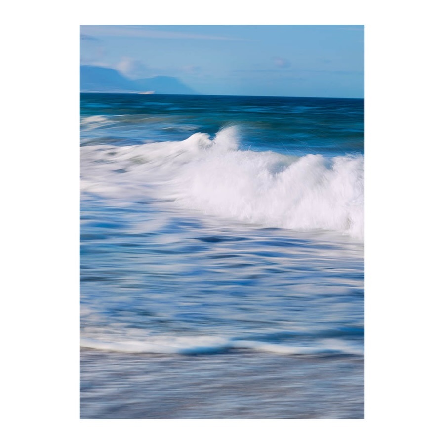 Abstract image of ocean waves crashing on the shore with a blurred effect, creating a sense of motion and tranquility under a blue sky.
