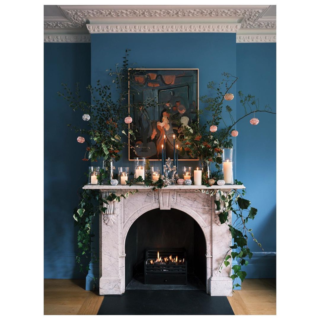 Living room interior featuring a fireplace mantel adorned with foliage, candles, and a painting, showcasing a cozy and inviting atmosphere.