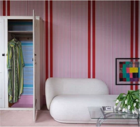 Interior shot featuring a white curved sofa against pink and red striped wallpaper by photographer James Merrell.