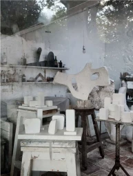White sculptural plaster models on wooden stools and tables in an artist studio shot by James Merrell