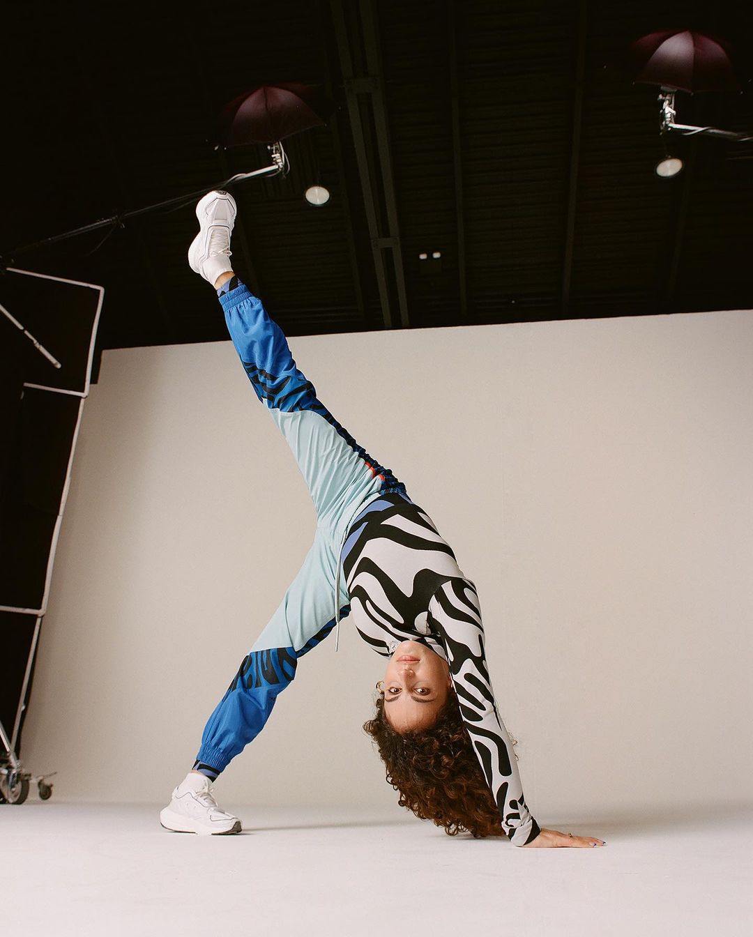Young woman in activewear strikes a yoga pose indoors, showcasing balance and flexibility against a clean backdrop in a studio setting.