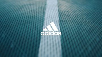 Close-up of the Adidas logo on a textured light blue background with a white stripe down the center, suggesting a sportswear product.
