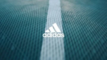 Close-up of the Adidas logo on a textured light blue background with a white stripe down the center, suggesting a sportswear product.