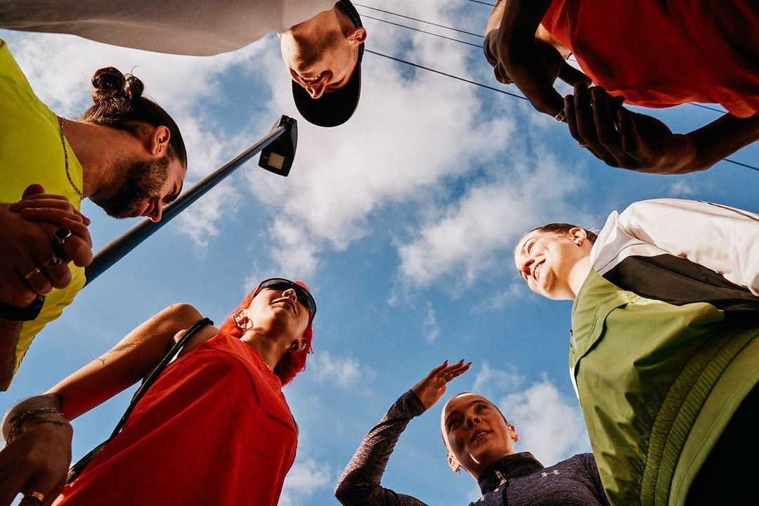 Low-angle shot of six diverse adults in casualwear against a cloudy sky, creating a cheerful, collaborative, and inclusive vibe.