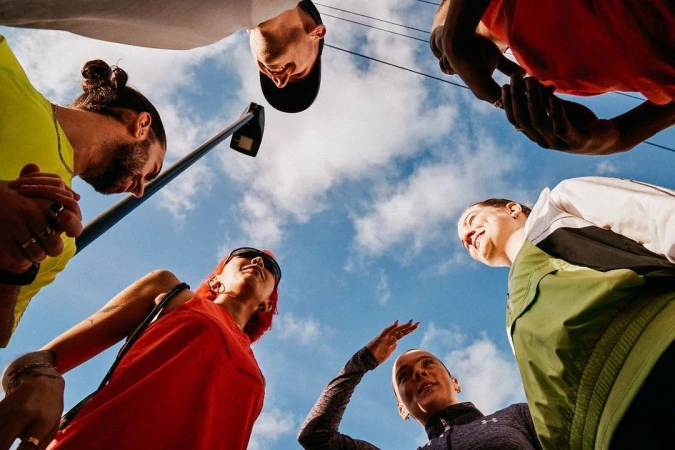 Low-angle shot of six diverse adults in casualwear against a cloudy sky, creating a cheerful, collaborative, and inclusive vibe.