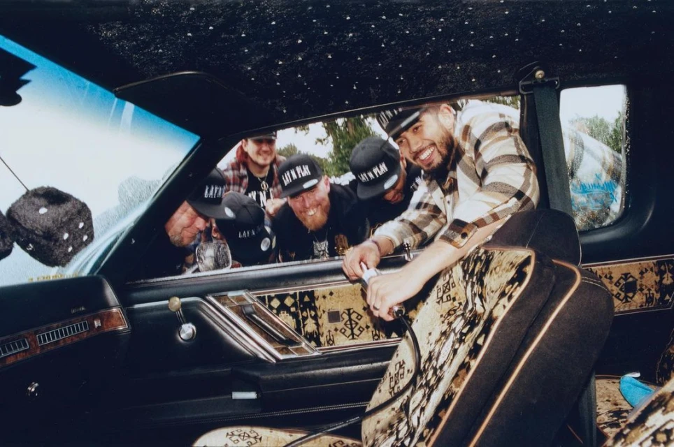 Group of five young adult males inside a vintage car, posing and smiling, with visible dice hanging from the rearview mirror.