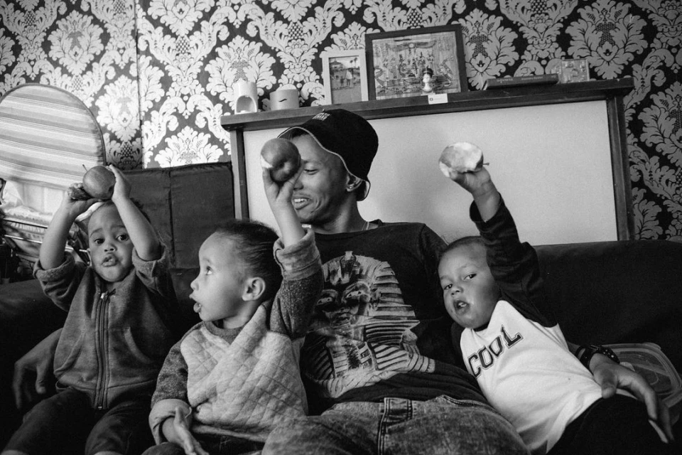 Black-and-white photo of a woman sitting on a couch with three children holding apples, with a patterned wallpaper in the background.