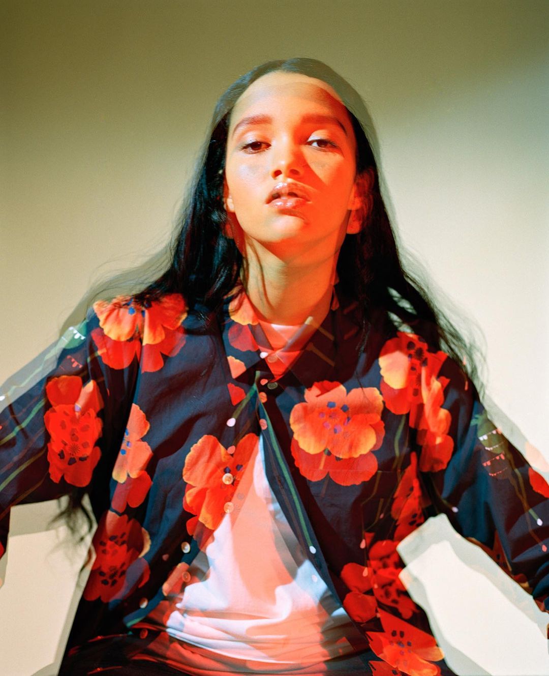 Portrait of a young woman with dark hair and a floral shirt against a neutral backdrop with superimposed light effects, fashion photography.