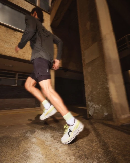 Athletic man in running shorts and long sleeve top runs in athletic shoes down a city street at night with blurred motion.