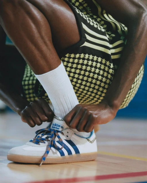 Close-up shot of an Adidas shoe being tied by an African American person in a patterned outfit on an indoor court.