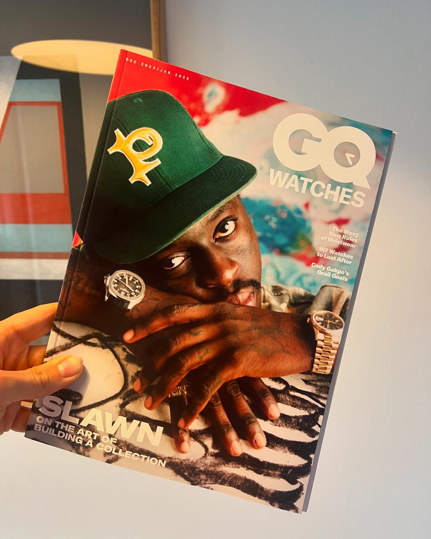 GQ Watches magazine cover featuring a man in a green cap and watches, held in a person's hand, with geometric art in the background.